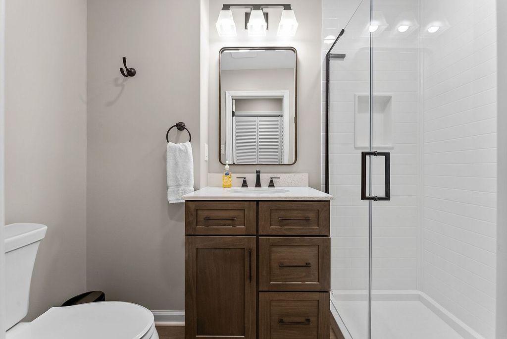 This Custom Venetia Guest Bathroom with a Spacious Walk-In Shower Covered in Glass, Warm Wood Vanity, Quartz Countertop Combines a Sleek, Modern Design with Timeless Finishes.