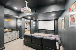 A cozy Sewickley home movie theater with a large screen, black leather couch, and cabinetry; dark walls and light carpet create an intimate setting.
